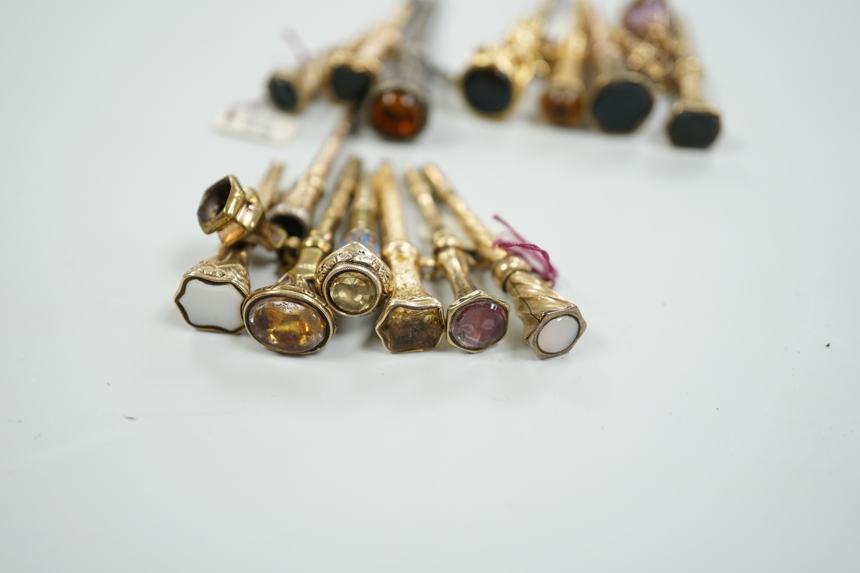 Fifteen assorted 19th century mainly yellow metal overlaid and gem set watch keys, including bloodstone, citrine and white chalcedony and one with enamel, mostly of trumpet form, largest 51mm.